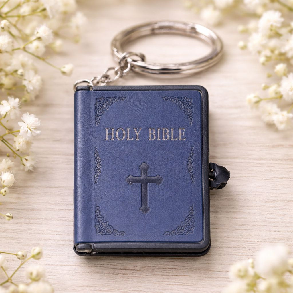 Blue Holy Bible keychain with cross design on a light background with white flowers.