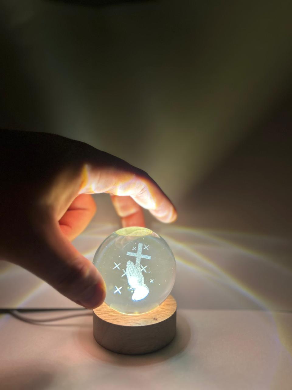 Hand holding a glowing crystal ball with a cross symbol on a dark background