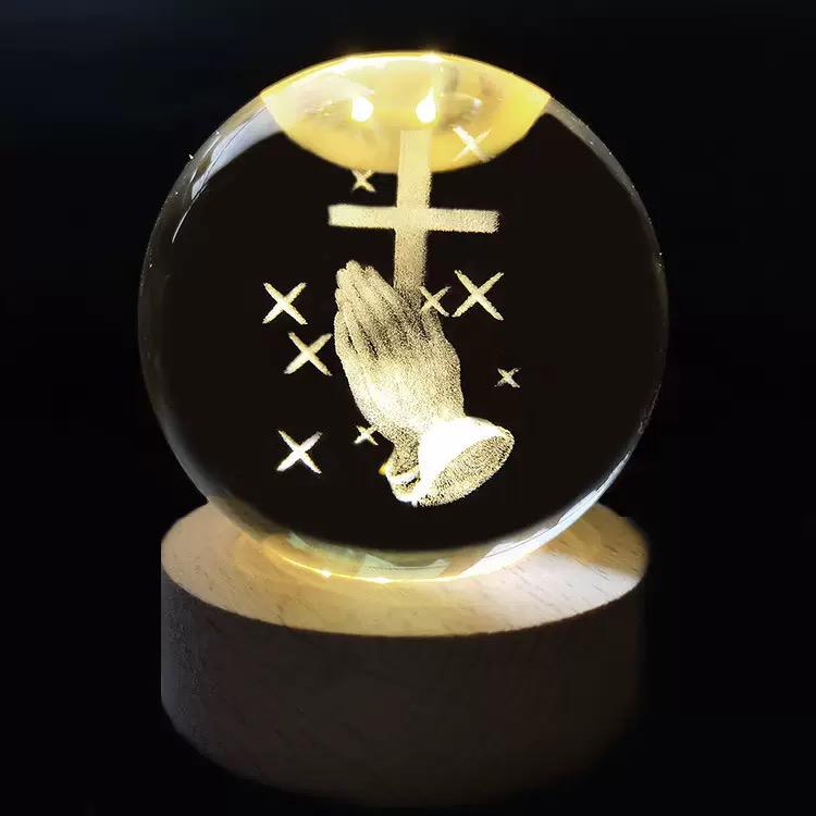 Crystal ball with engraved cross and praying hands on a dark background