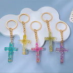 Five cross-shaped keychains with colorful decorations on a white cloud-shaped stand against a light blue background.