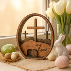 Wooden Easter decoration with cross and 'He is Risen!' text, surrounded by Easter eggs and a rabbit figurine.