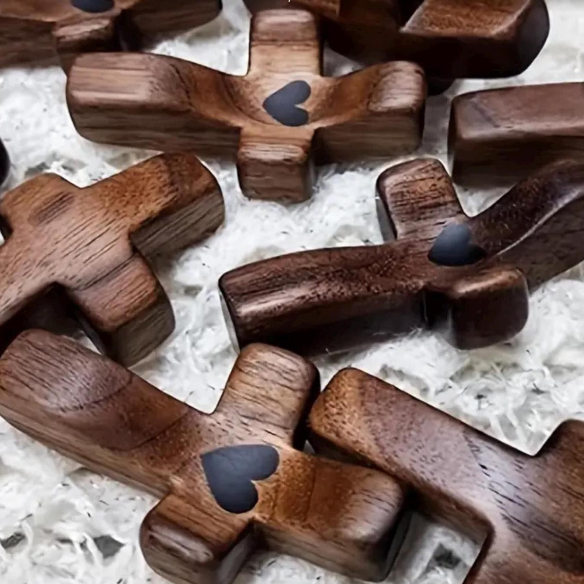 Several dark brown wooden cross pendants with a small heart-shaped cutout, arranged on a white textured fabric background.